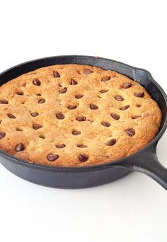 a chocolate chip cookie in a cast iron skillet on a white table with a spoon