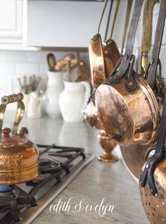 copper pots and pans hanging from the ceiling in a kitchen with marble counter tops