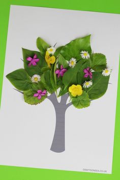 a paper cut out of a tree with flowers and leaves on the top, in front of a green background