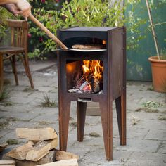 a person is holding a stick over an outdoor wood stove with firewood in it