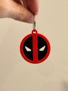 a hand holding a red and black deadpool keychain with eyes on it