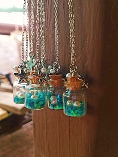 three glass jars filled with blue and green beads hanging from a wooden wall next to a chain