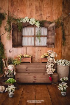 an arrangement of flowers and stuffed animals in front of a wooden wall with windows on it