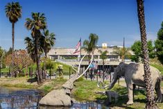 an elephant and its baby are standing in the water near some palm trees, while people look on