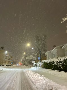 a snow covered street at night with cars parked on the side and buildings in the background