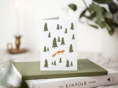 a card with an orange fox on it sitting next to some books and a candle