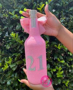 a woman holding up a pink bottle with the number 21 on it and a bow