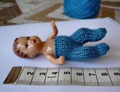 a toy doll laying on top of a table next to a measuring tape and yarn