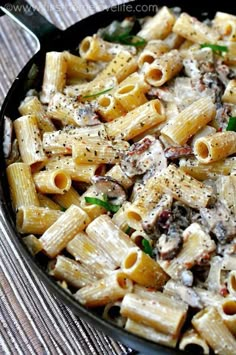 a skillet filled with pasta and mushrooms on top of a wooden table next to a fork