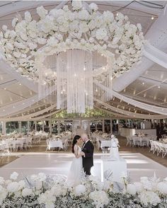 a bride and groom standing under a chandelier in a ballroom with white flowers