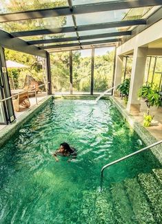 a woman swimming in a large indoor pool surrounded by greenery and glass walls,