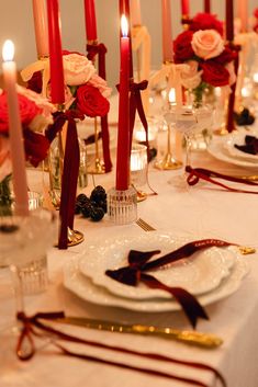 the table is set with white plates and red roses in vases, candles and napkins