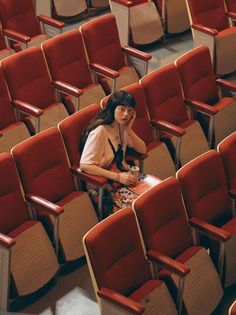 a woman is sitting in the middle of a row of empty red and beige chairs