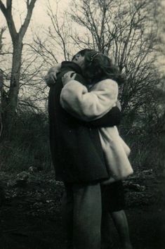 an old black and white photo of two people hugging each other in front of trees