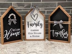 three small houses with signs on them sitting next to each other in front of a brick wall