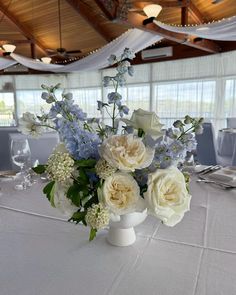 a vase filled with white and blue flowers sitting on top of a dining room table