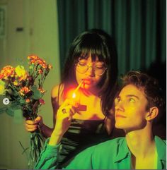 a woman lighting a candle on a man's face with flowers in front of her