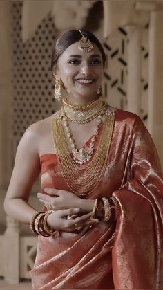 a woman in an orange sari with gold jewelry on her neck and hands behind her back