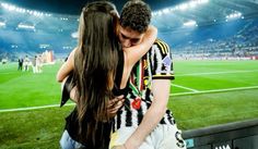 two people embracing each other in front of a soccer field with fans watching from the stands