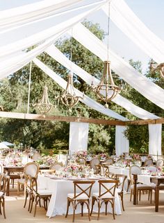 an outdoor wedding reception with white draping and chandeliers hanging from the ceiling