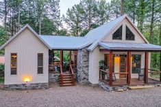 a small white cabin in the woods with stairs leading up to it's front door