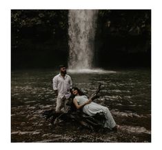 a man and woman standing in front of a waterfall