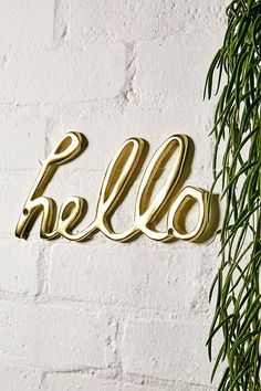 the word hello spelled in gold on a white brick wall next to a green plant