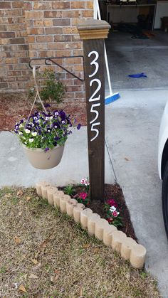 a wooden sign with flowers hanging from it's side in front of a brick building