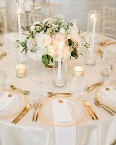 the table is set with white and gold plates, silverware, and flowers in vases