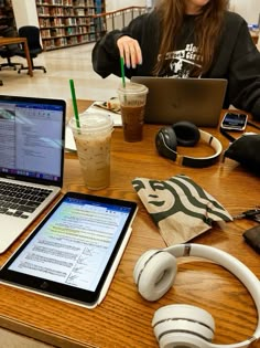 a woman sitting at a table with two laptops and headphones on her desk