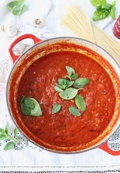 a red pot filled with sauce and basil leaves