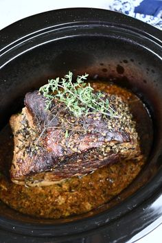 a piece of meat sitting in a crock pot with some herbs on top of it