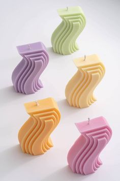 four candles with different shapes and colors on white background, one candle is shaped like a wave