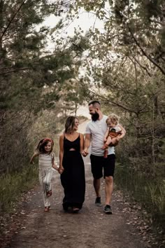 a man, woman and two children walking down a dirt path in the woods holding hands