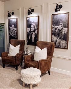 two brown chairs sitting next to each other in front of three framed pictures on the wall