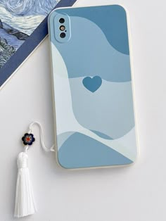 an iphone case with a heart on it next to a tassel