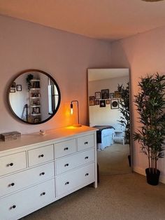 a room with a dresser, mirror and potted plant