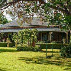 the house is surrounded by lush green grass and trees, with bushes in front of it