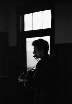 a man standing in front of a window holding a guitar