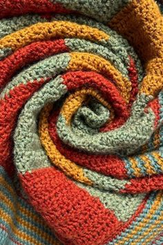 a multicolored crocheted blanket is folded in the shape of a spiral