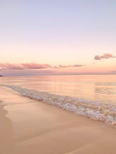 an ocean beach with waves coming in to the shore and pink clouds above it at sunset