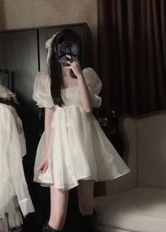 a woman in a white dress and black boots is looking into a mirror with a mask on her face