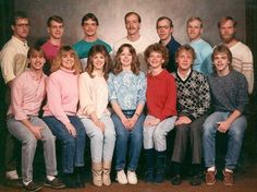 a group of people sitting next to each other in front of a gray wall with one person standing