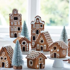 a group of gingerbread houses sitting on top of a white cake plate next to trees