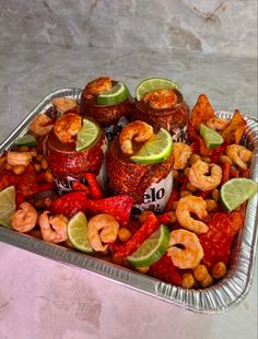 a tray filled with shrimp and other foods on top of a marble countertop next to lime wedges