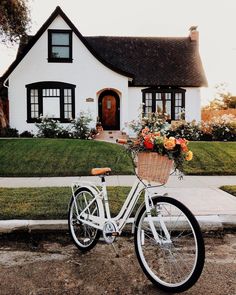 a bicycle parked in front of a white house with flowers on the handlebars