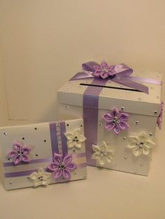 two white boxes with purple ribbons and flowers on them, one has a gift box in the shape of a present