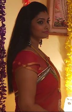 a woman in a red sari standing next to a wall with flowers on it