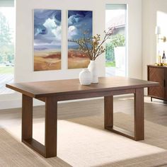 a large wooden table with two paintings on the wall behind it and a vase filled with flowers