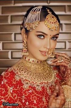 a woman in a red and gold bridal outfit holding her nose ring up to her mouth